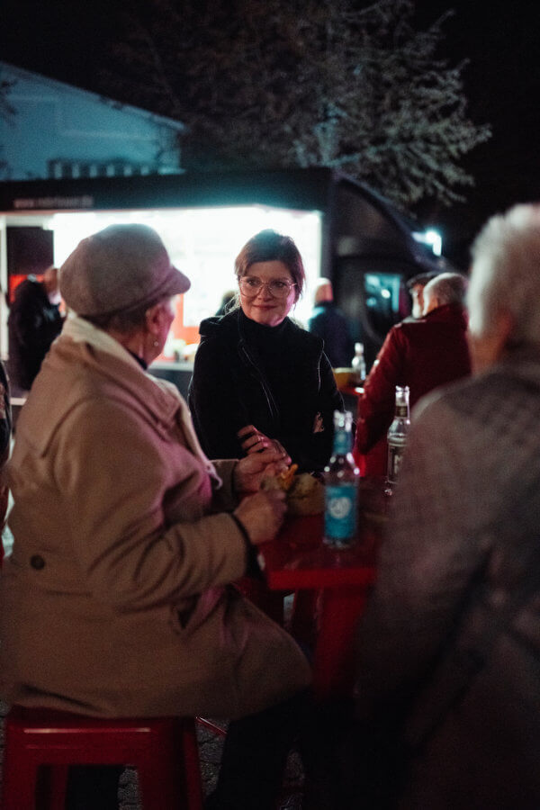 Frau im Gespräch mit Besuchern am Tisch