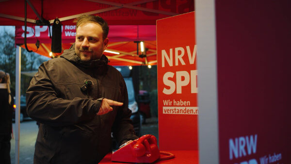 Mann zeigt auf rotes Telefon am NRWSPD-Stand